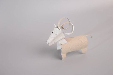 Geri dönüşümlü tuvalet kağıdı rulolarından sevimli koçbaşı ya da boynuzlu sığır zanaatı yapmak için özel ders. Çocuklar ve anaokulu öğrencileri için ideal, yaratıcılığı teşvik etmek ve motor becerileri geliştirmek, gri yüzeydeki biblo