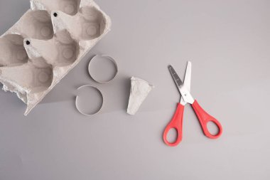 Minimalist DIY proje sahnesi: gri bir masaya yerleştirilmiş boş yumurta kutusu. Parçalanmış kağıt halka, kağıt koçbaşı yapmak için kullanılan mukavva tabanlı kursun bir parçası. Sanat meraklıları için ideal 
