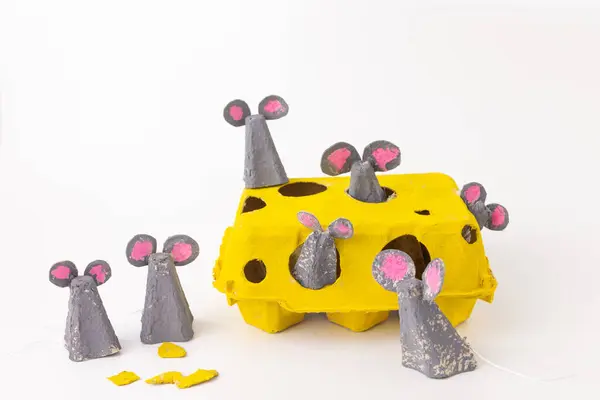 stock image Yellow egg carton creatively repurposed as cheese with mouse figurines peeking out. Gray and pink paper used for mice with tails. Playful scene showcases imaginative crafting