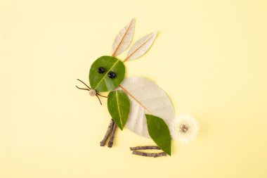 Sade sarı arka planda doğal malzemelerden yapılmış tavşanın yaratıcı bir temsili. Yeşil yapraklar gövdeyi ve kafayı, dallar bıyıkları ve bacakları, ve karahindiba da kuyruğu oluşturur. Sanatsal, doğa zanaatı
