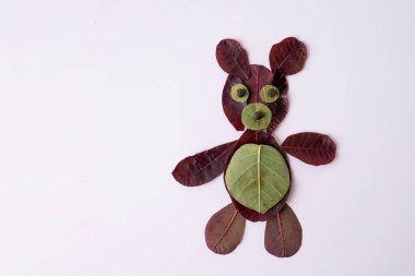 Creative depiction of teddy bear made from leaves on white surface. maroon vegetable foliage for ecological art. Perfect nature craft project for kids, emphasizing natural materials and creativity. clipart