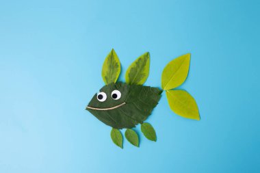 Artistic representation of fish using leaves and natural materials. Large green leaf body, googly eyes, and smiling twig mouth. Showcases creativity and resourcefulness in kids' craft and natural art. clipart