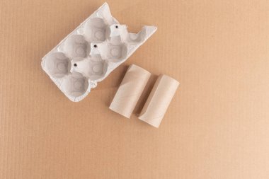 Geri Dönüşümlü Malzemeler: Yumurta kutusu ve tuvalet kağıdı rulosunun yer aldığı minimalist düz yer. Kahverengi el işi kağıt arkaplanda üst görünüm