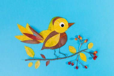 A charming craft of a bird perched on a branch with leaves and berries, made from autumn dry leaves. Creative nature art. clipart