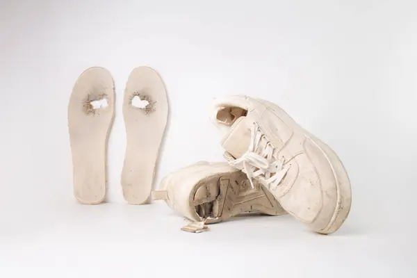 stock image  a single worn out white sneaker with its sole partially detached and the insole completely removed. heavily used, with visible dirt and wear, The removed sole and insole are lying next to the sneaker