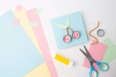Çocukça bir el işi projesinde kağıt üzerinde makas, mavi kiraz temalı kart şablonu sergileniyor. DIY ve sanatsal eğitim için harika