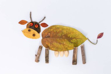 Doğal malzemelerden yapılmış yaratıcı bir sanat eseri. Hayvan figürü, yapraklardan, dallardan ve tohumlardan yapılmış bir inek. Kahverengimsi sarı yaprak gövde, daha küçük sarı yaprak başı, dal bacaklar.