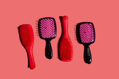 Bir dizi plastik saç fırçası, yumuşak pembe arka planda, üst manzarada düzgün sıralanmış. Fırçalarda değişik şekiller, boyutlar ve tasarımlar gösteriliyor, farklı saç tipleri ve şekillendirme ihtiyaçları için..