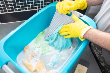 Evde el yıkama, kirleri ve lekeleri temizlemek için taşınabilir bir çamaşır tahtası kullanan bir adam. Kesilmiş bir fotoğraf.