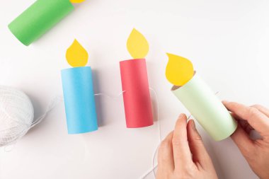 threading string final garland, step-by-step making a paper candle garland using cardboard tubes, DIY craft tutorial, hands holding needle with thread, step in creative process clipart