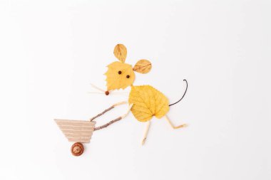 Sarı sonbahar yapraklarından yapılmış bir fare beyaz arka planda kartondan yapılmış bir el arabası, dallar ve bir palamut itiyor. Kopya uzayı ile minimalist düz konum. Sonbahar ve doğa zanaatı 