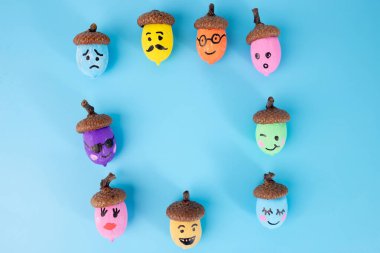 Emoji mavi arka planda renkli boyalar içinde meşe palamudu ile karşı karşıya. Düz sonbahar sanatı fikri, tebrik kartları, posterler, afişler ve yaratıcı DIY projeleri için idealdir. Eğlence ve şenlik havası.