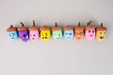 Açık gri arka planda çeşitli yüz ifadeleri olan renkli meşe palamutları. zanaat projeleri ve sonbahar dekorasyonları için DIY sürecinde adım. 