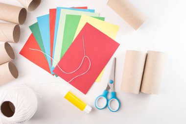 renkli kağıt kağıtlar, boş karton tüpler, mavi saplı makas, beyaz tel top, yapıştırıcı çubukları, el işi materyalleri, sanat ve zanaat aktiviteleri, adım adım görsel rehber, eğlenceli eğitim aktivitesi, 