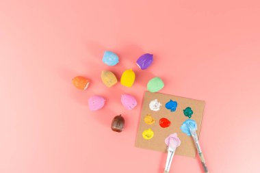 Resmedilmemiş meşe palamudu, boya paleti ve pembe arka planda fırçaların yanında emoji yüzlü birkaç meşe palamudu. Kartlar için düz sonbahar sanatı fikri, DIY doğa sanatı projesi, sonbahar süslemesi, ders