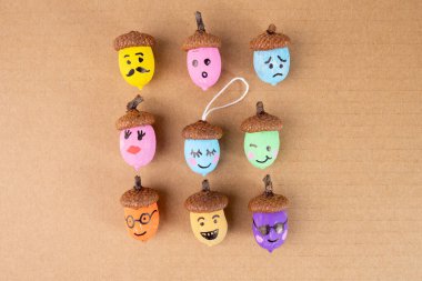 Kahverengi arka planda yüzleri olan canlı meşe palamutları. Eğlence amaçlı DIY zanaat fikirlerini, mevsimsel dekorasyon ilhamını ve yaratıcı sonbahar temalı tasarım projelerini vurgulamak