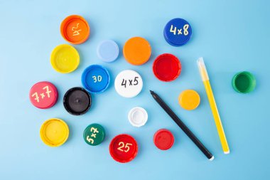  Çarpma egzersizleriyle şişe kapakları, mavi arka planda kalemler, çocuklar için pratik, düz konsept. Yaratıcı süreçte adım at, DIY, öğrenmek için etkili, usta çarpım tabloları.