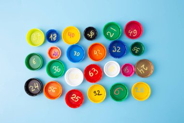 Mavi arka plan çarpma egzersizleriyle renkli şişe kapakları, düz konsept, matematik öğrenimi, çocuklar için sınıf matematik aktivitesi, çarpım tablosu uygulaması, ev matematiği. 