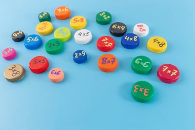 Mavi arka planda çarpma problemleri olan renkli şişe kapakları. Matematik öğrenme ve sınıf aktiviteleri için düz yatay eğitici konsept, yaratıcı süreçte adım, DIY, pratik