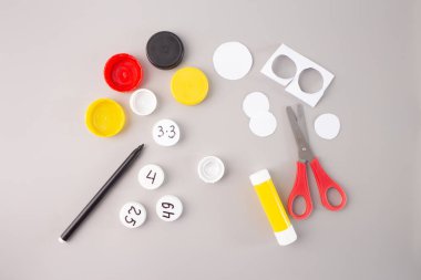 plastic bottle caps with hand-written numbers and multiplication facts on a gray background. glue, scissors and marker, step in creative DIY process, Educational math activity for kids  clipart