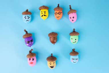 Mavi arka planda çeşitli yüzlerle boyanmış renkli meşe palamudu seti. Düz kompozisyon. Sonbahar gemisi ve DIY proje konsepti. yaratıcılık sürecinde adım, öğretim, üst görünüm