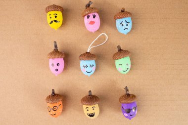 Kahverengi arka planda anlamlı yüzleri olan meşe palamutları. Sanatsal zanaat fikirleri sergilemek, sonbahar tasarımları, DIY kavramları ve yaratıcı mevsimsel projeler için mükemmel. Üst görünüm