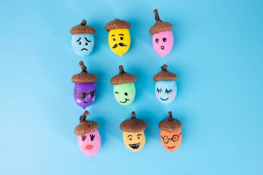 Mavi arka planda çeşitli emoji yüzleriyle boyanmış renkli palamutlar. Düz kompozisyon. Sonbahar gemisi ve DIY proje konsepti. Tebrik kartları, posterler ve afişler için tasarım