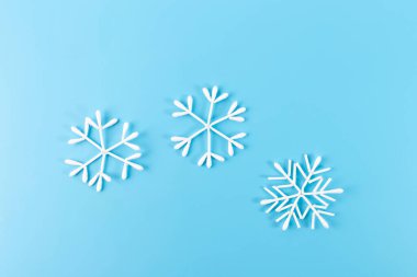 Pamuklu çubuklardan yapılan kar taneleri mavi arka planda asılı duruyor. Minimalist kış dekorasyonu. Noel ve kış tatili konsepti.
