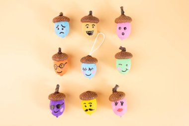 Şeftali arka planında anlamlı yüzleri olan meşe palamutları. Sanatsal zanaat fikirleri sergilemek, sonbahar tasarımları, DIY kavramları ve yaratıcı mevsimsel projeler için mükemmel. Üst görünüm