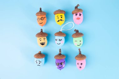 Mavi arka planda sıralanmış yüzlü palamutlar, çeşitli renkler ve ifadeler, yaratıcı sanatlar, eğitim, sanatsal, sonbahar, doğa, yaratıcı süreçte adım, çocuklar için özel ders.