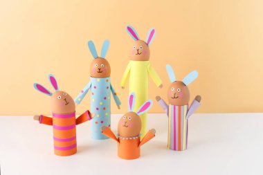 Handmade Easter bunny crafts using colored paper and eggs on a peach background. holder made of recycled toilet paper roll. Easter celebration and DIY craft concept. soft focus clipart