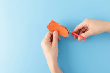 Yukarıdan aşağıya bakan eller, yengeç zanaatı projesinin yaratıcı bir parçası olan bacaklara, pençelere ve gözlere portakal kağıdı parçaları ya da karton parçaları kesiyor. mavi arkaplan, eğlenceli oyuncak