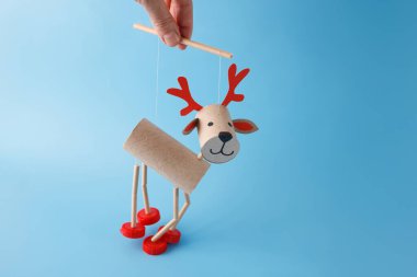 Hand holding DIY reindeer puppet made of cardboard tubes, red plastic caps, Christmas craft and holiday decoration concept, easy activity to do, toilet paper roll craft for kid, marionette clipart