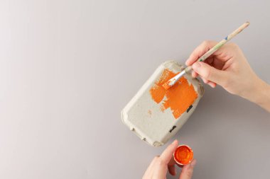 Gri bir arka planda DIY projesi için fırçayla yumurta kartonunu turuncuya boyamak. El işçiliği devam ediyor. Yaratıcı geri dönüşüm ve çocuk etkinliği kavramı.