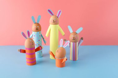 El yapımı Paskalya tavşanları ailesi pembe ve mavi arka planda geri dönüşümlü karton tüpler kullanıyor. Paskalya kutlaması konsepti, çocuklar için bahar etkinliği, eğlence ve yaratıcılık için DIY zanaatı.