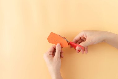 Eller turuncu kağıdı kırmızı makasla sarı arka planda yengeç pençesi şeklinde keser. DIY zanaat süreci
