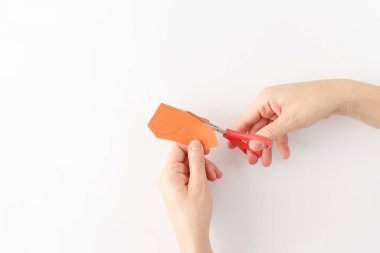 creative process in progress, Hands cutting orange paper into crab claw shape with red scissors on a white background. DIY project. Creative recycling and easy kids activity concept clipart