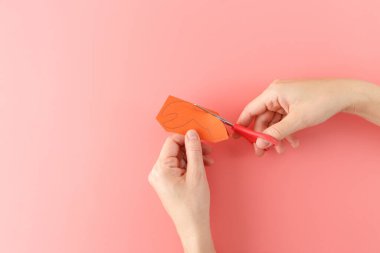 Eller turuncu kağıdı kırmızı makasla pembe arka planda yengeç pençesi şeklinde keser. DIY zanaat süreci