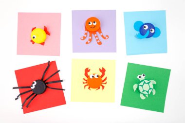 DIY yaz kağıtları ve plastik kapaklar çocuklar için, günlük geri dönüştürülmüş eşyalardan nasıl basit hayvanlar yapılacağı, ev yapımı renkli kare kağıtlar, üst görünüm, beyaz arka plan, anaokulu saatleri 