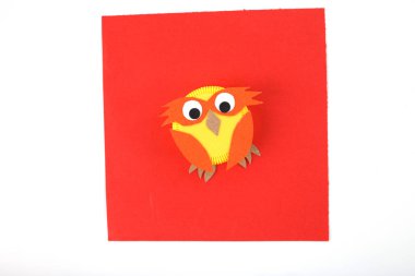 Plastik kapaklı bebek oyunu, kırmızı kare kağıtta kullanılmış plastik şişe kapağından yapılmış baykuş, çocuklarla oynamak, komik sanat projeleri, geri dönüşümlü materyal konsepti, çocuklar için ders imajı.