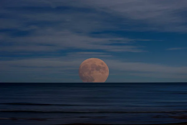 Photo of the moon rising over the sea. Illustration. calm water with moving effect, dark moving clouds, photo as a drawing