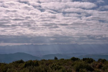 Bulutlu ve güneşli dağ manzarası. Bulutların arasında çalılar, güneş ışınları. İnsanlar yok, boşluk, çizgiler, gölgeler, berraklık.