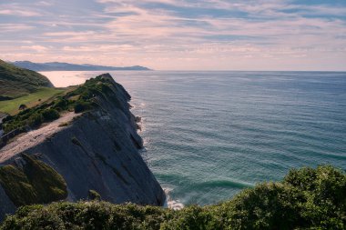Rock formations on the coast of Zumaya, Spain.Sunny day, empty beach, cottage, boat sl clouds, vegetation. Flysch. San Telmo Chapel