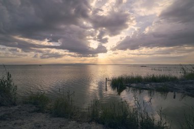 Bulutların arasında Valencia gölünde gün batımı. Sazlıklar, yansımalar, sakin sular, Akdeniz gelenekleri ve ekosistem.,