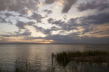 Bulutların arasında Valencia gölünde gün batımı. Sazlıklar, yansımalar, sakin sular, Akdeniz gelenekleri ve ekosistem.,