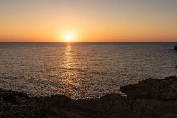 Şafakta ya da alacakaranlıkta sakin ve sakin deniz. Turuncu gökyüzü, berrak gökyüzü, sakin sular, kayalar, boş uzay, Akdeniz..