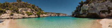 Menorca, Balearic Adaları, İspanya 'daki Cala Macarelleta' nın panoramik görüntüsü. Boş bir sahil, bulutsuz, kayasız, turkuaz su, beyaz kum, kıyıdaki kayalar ve açık alan..