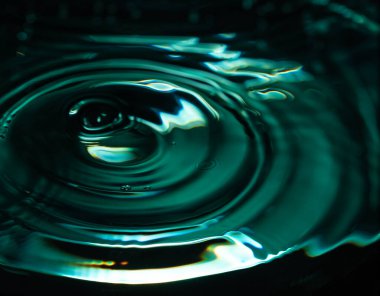 402.Sıvı yüzeye yakın çekim, çarpışmadan dolayı oluşan dalgalanma halkalarını gösteriyor. Teal ve koyu yeşil ışık soyut dalga desenleri oluşturur. Işıklar ve gölgeler akışkan hareket ve dokuyu vurgular.