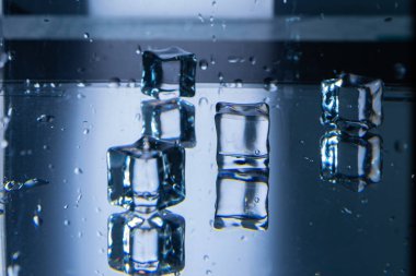 3.Kübik buz küpleri koyu, ıslak ve yansıtıcı bir yüzeyde. Yansımalar, derinlik ve simetri. Su damlacıkları yüzeyde görülebilir. Arka plan koyu, yüksek kontrastlı ve soğuk atmosferli..