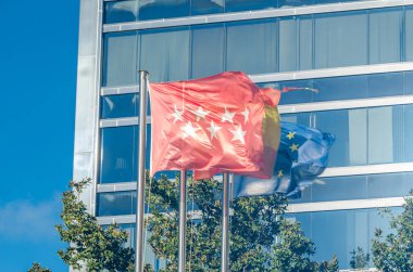 MADRID, SPAIN - DECEMBER 27, 2021: Flags of the Community of Madrid, Spain and the European Union in front of the Acerinox headquarters in Madrid, Spain. Acerinox is a stainless steel manufacturing conglomerate group based in Spain